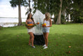 Load image into Gallery viewer, Two women holding fresh citrus beside a skirted Tree Defender protecting a young tree near a Florida lake.