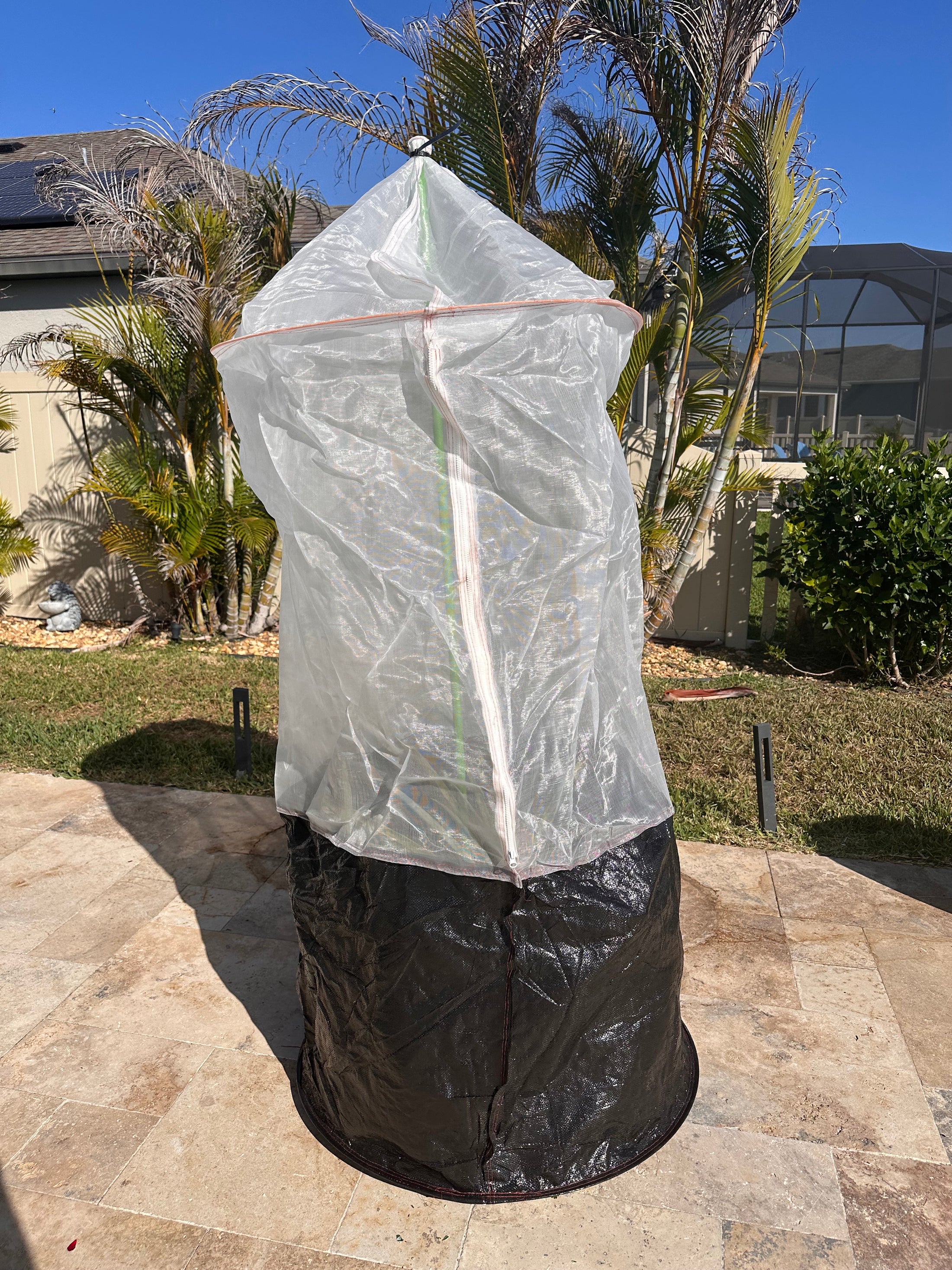 Skirted Tree Defender with a white breathable mesh cover, built-in front zipper, and black skirt secured around the base of a young tree.